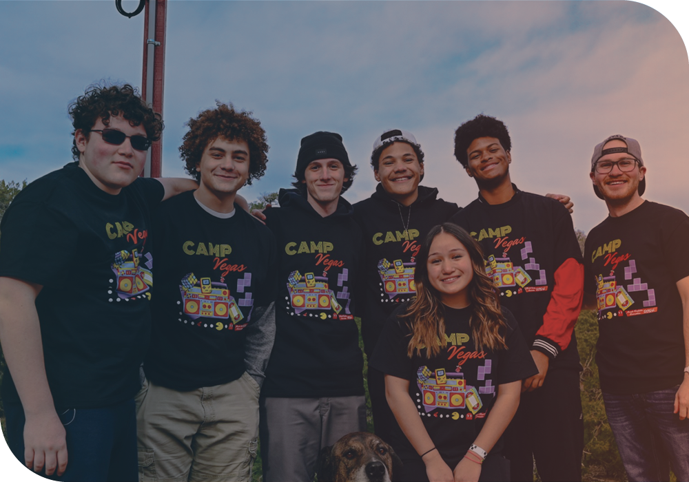 A group of seven young students smiling together for a photo at Camp Vegas. There is also a dog sitting and posing for the photo.