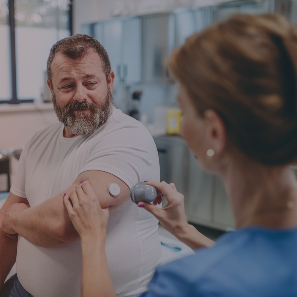 A man is at the doctor getting blood glucose sensor placed on his arm.